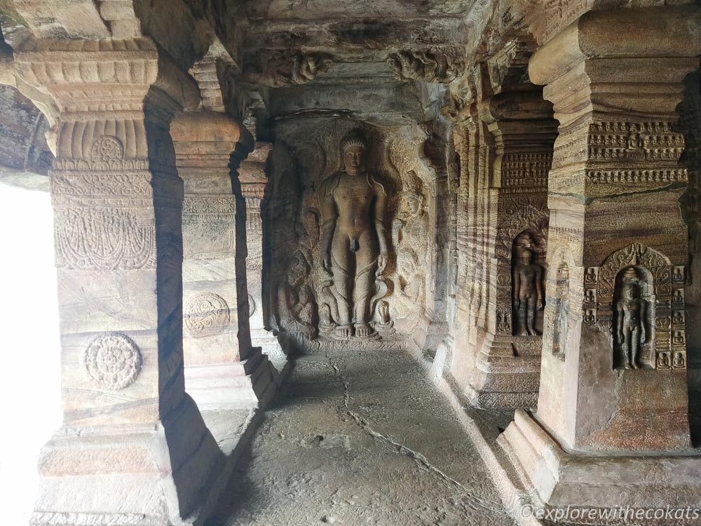 Sculpture of Bahubali, standing in a meditative posture with vines wrapped around his leg and pillars with intricate sculptures